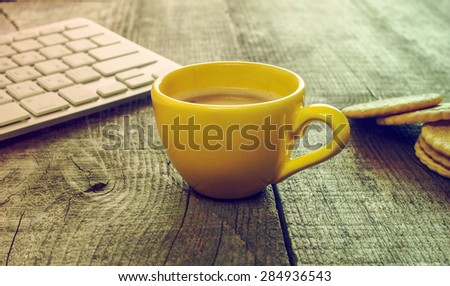 Computer keyboard, cup of coffee and biscuits on old weathering wooden table. Grunge style
