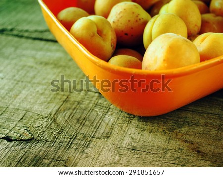 Fresh apricots in orange bowl on wooden weathering table. Grunge style