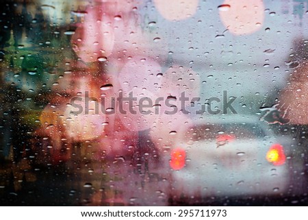 Driving in rain, raindrops on car window with light bokeh, rainy season abstract background.