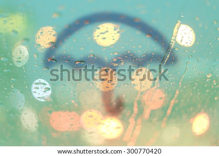 Rain drops and umbrella write on window with light bokeh, rainy season abstract background.