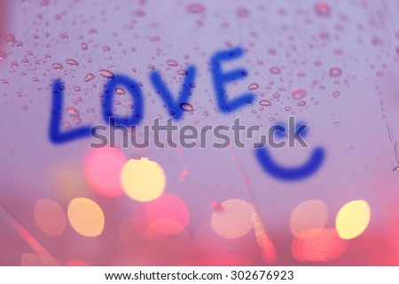 Rain drops and the word love write on window with light bokeh, rainy season abstract background.