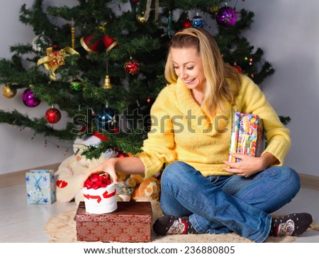 Attractive young woman holding gift and sits near Christmas tree