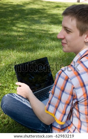 Young man sitting on green grass in park and types on laptop