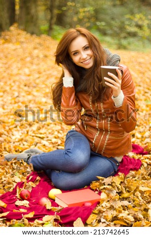Happy young woman with book and apples in the autumn park