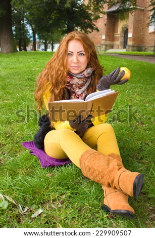 Happy young woman with book and apple in the autumn park