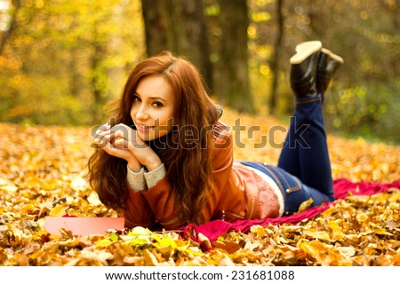 Happy young woman with book and apple in the autumn park
