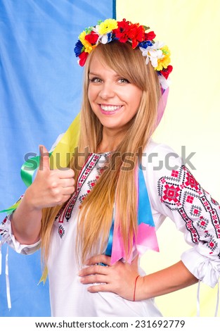 Happy cute girl in the Ukrainian national costume with thumbs up gesture and Ukrainian flag