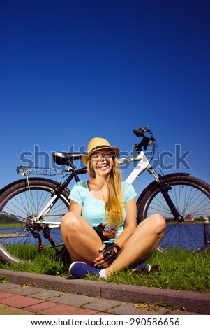 girl listening music from a smart phone sitting with a bike on the beach