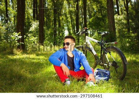 young man sitting in the park  and resting after bicycle ride