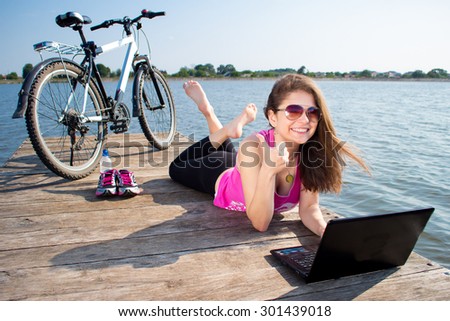 young woman in pink shirt lying on the lake bridge using laptop computer