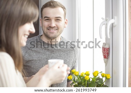 Happy couple standing in sunshine by the window with coffee