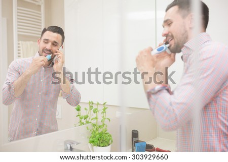 Attractive Latin man having phone conversation during brushing teeth.