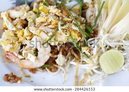 Seafood pad Thai dish of Thai fried rice noodles on a square white plate with chopsticks and grated carrot garnish.