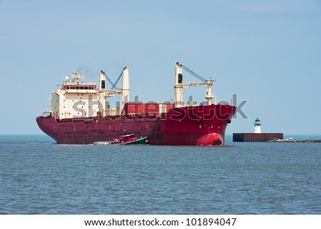 A harbor tugboat helps a large ocean going freighter turn left around a navigation beacon at the entrance to harbor at the Port of Cleveland, Ohio from Lake Erie