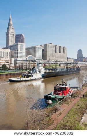 The 2012 Great Lakes shipping season gets underway as a tugboat and barge sail up the Cuyahoga River past the Tower City Complex in Cleveland, Ohio as a moored small tug awaits her next assignment