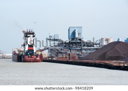 A stern view of an articulated tugboat and barge docked at the Cleveland Bulk Terminal in the Cleveland Harbor on Lake Erie,  The boat is taking on iron ore to be delivered to a steel mill