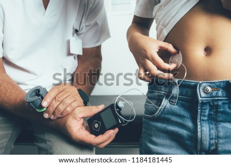Cropped view of a diabetic child applying an insulin pump dressing in his abdomen with the doctor in the clinic. Child diabetes concept