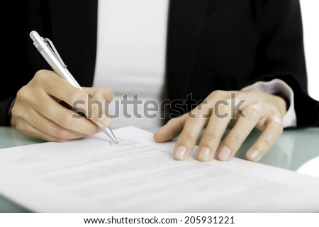 closeup of a woman hands signing a document - focus on the right hand and the pen