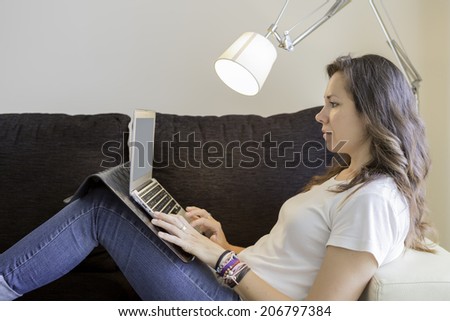 profile of a young woman lying on a sofa using a laptop - focus on the face