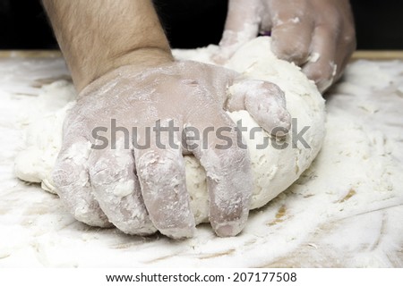 closeup of hands kneading bread on a wooden board - focus on the index finger