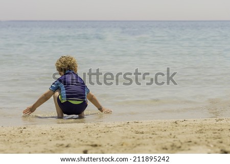 crouched child playing with the water on the seashore his back to the camera - focus on the child