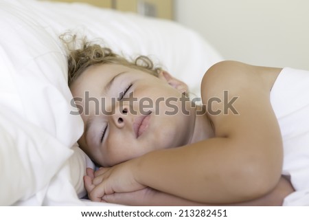 closeup of a cute little boy sleeping sideways in bed with entwined hands below the face - focus on the face