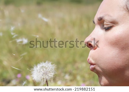 closeup of a profile of a face of a young woman blowing a dandelion on a grass background - focus on the face
