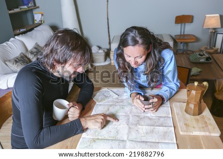 couple of hikers planning the route sitting around a table pointing the route in a map in a welcoming shelter - focus on the young woman