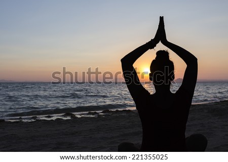 backlight of a woman practicing yoga sitting on the shore of the beach at sunset