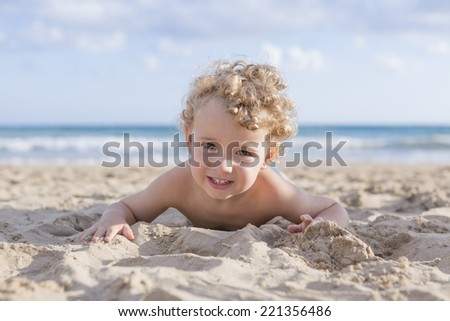 cute smiling blond boy lying on the sand on the beach looking at camera - focus on the face