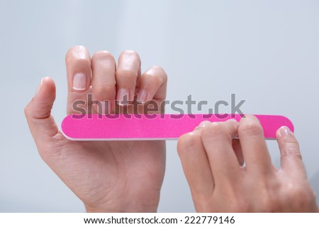 closeup of hands of a young woman filing her nails with french manicure with a pink nail file - focus on the middle finger of the left hand