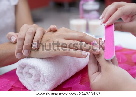 closeup of the hands of a young woman receiving the nail file by a beautician at the beauty salon - focus on the middle finger