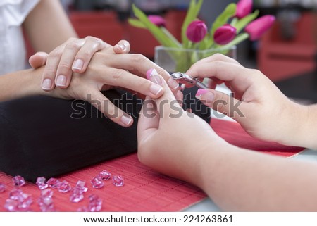 detail of the hands of a beautician removing the cuticles with a nipper to a young woman on a beauty salon - focus on the cuticle nipper