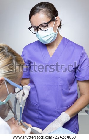 young female assistant helps on the work of the young female dentist on a dental cleaning at the dental cabinet