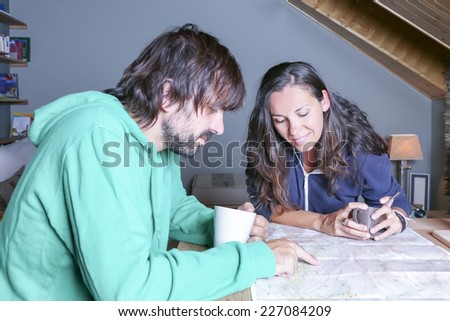 couple of hikers planning the route drinking coffee pointing the route in a map in a welcoming shelter - focus on the young woman