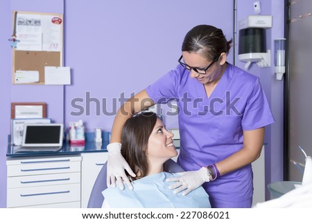 female assistant of a dental clinic smiling is calming female patient sitting on the dental chair of the cabinet before starting a checkup