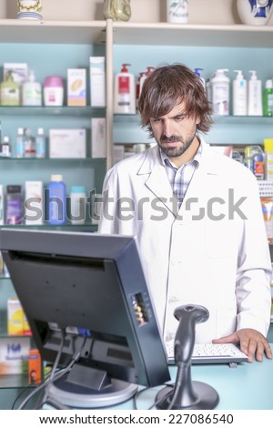 young male pharmacist working with the computer in the pharmacy standing looking at the screen