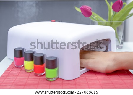 closeup of a uv lamp with a female hand inside fixing the gel nail polish at the beauty salon