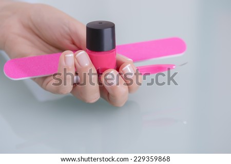 closeup of the hand of a young woman holding a pink nail polish, a pink nail file and a pink cuticle remover