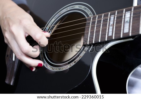detail of the hand of a young woman holding a guitar pick near the rosette playing a black acoustic guitar - focus on the pick