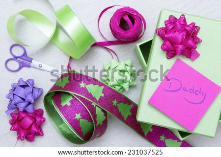 set of tools to wrap a christmas gift consisting of a green box, scissors, ribbons, bows and a post it with daddy word on a snow background