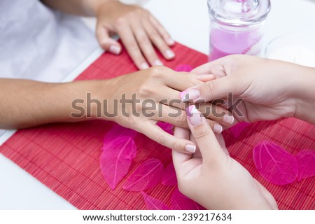 closeup of the hands of a young woman receiving a hand massage by a beautician on a beauty session at the nail salon - focus on the thumbs of the beautician
