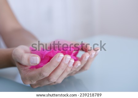 detail of the hands of a young woman holding pink flower petals - focus on the right index finger