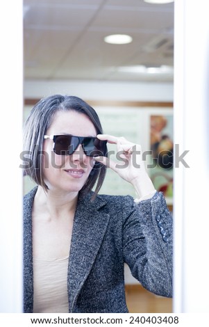 mirror image of a smiling young woman trying on sunglasses at optical shop - focus on the glasses center