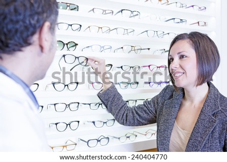 smiling young woman asking for advice to the optician and choosing glasses at the optical store - focus on the woman eyes