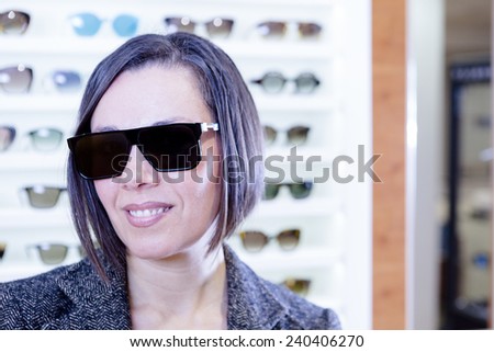 portrait of a smiling young woman at optical shop wearing very fashionable sunglasses with the sunglasses expositor at background - focus on the glasses center