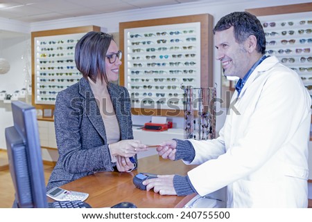 smiling young woman is paying with a credit card to a male optometrist at the optical shop - focus on the woman eye