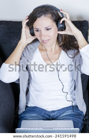 young woman enjoy listening music sitting on a sofa at home with headphones and laptop