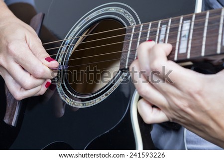 detail of a female hand holding a guitar pick near the rosette playing a black acoustic guitar - focus on the pick