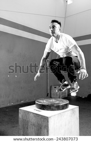 young male athlete doing a box jump at the gym - focus on the man